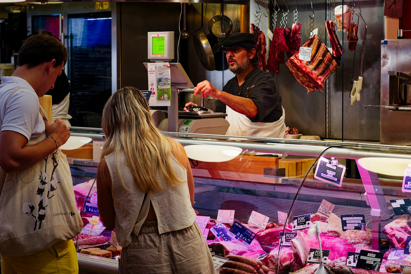 Butcher serves customers meat at a busy market counter.