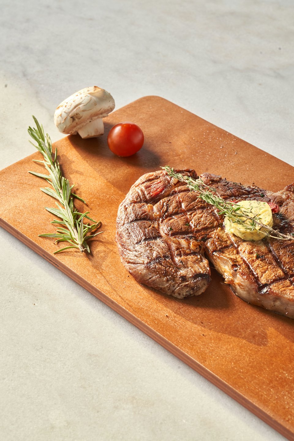 Grilled steak with herb butter and thyme on a wooden board.