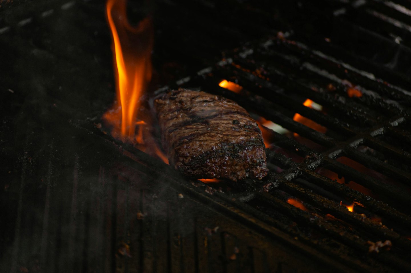 Thick steak searing on a hot grill with flames rising.