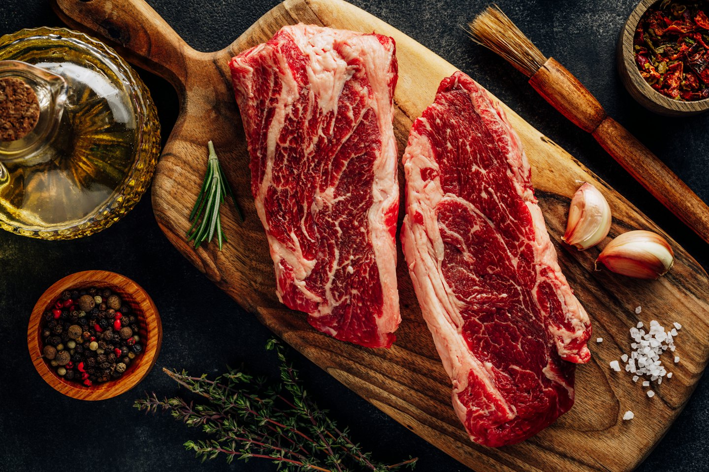 Two raw beef steaks on a wooden board with herbs and spices.