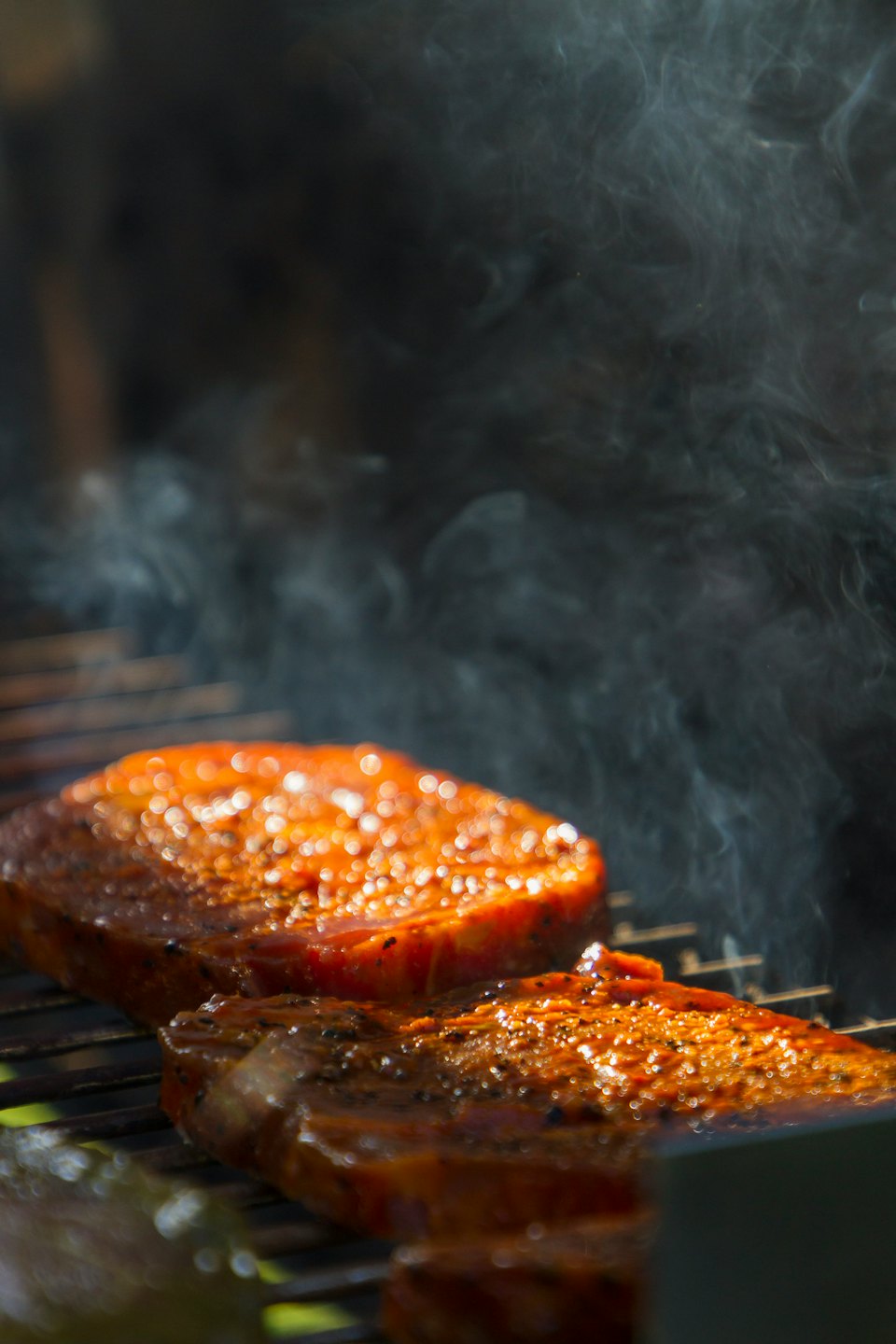 Marinated steaks cooking on a smoky outdoor grill.
