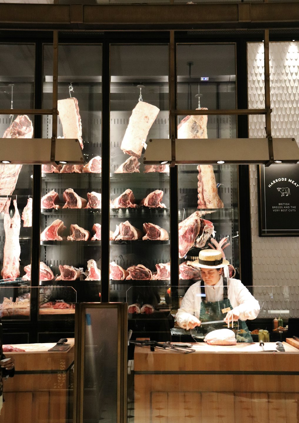 Butcher in apron cutting raw meat behind a market counter.