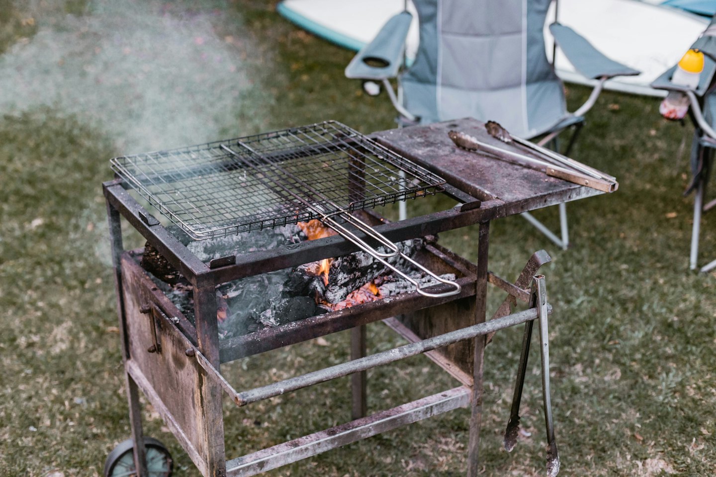 Rusty metal barbecue grill with glowing embers and rising smoke.
