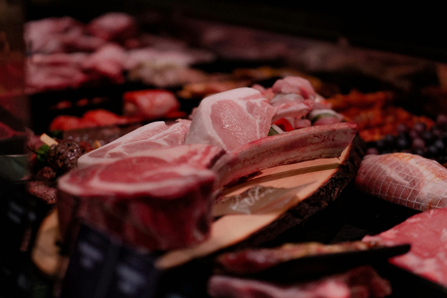 Raw steaks and ribs on wooden boards in a butcher case.