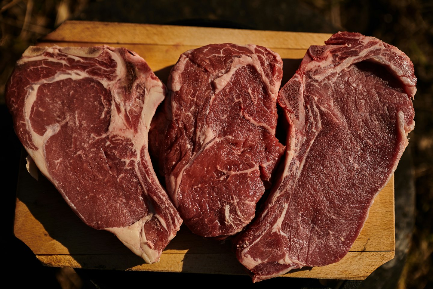 Three raw ribeye steaks on a wooden cutting board.