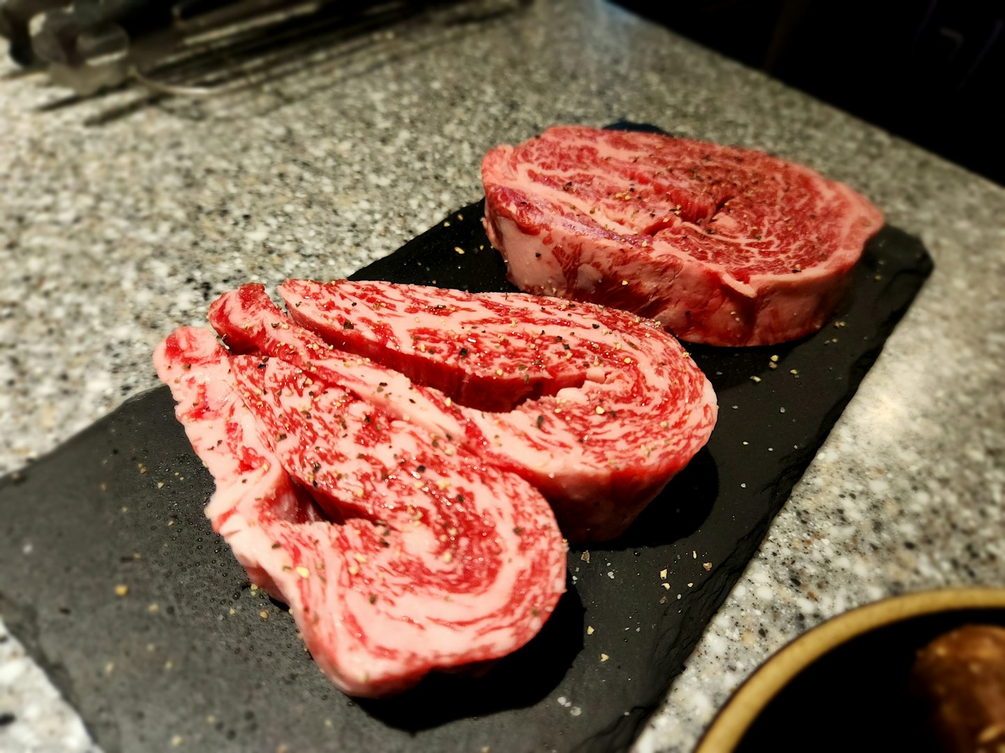 Seasoned marbled beef steaks resting on a dark slate board.